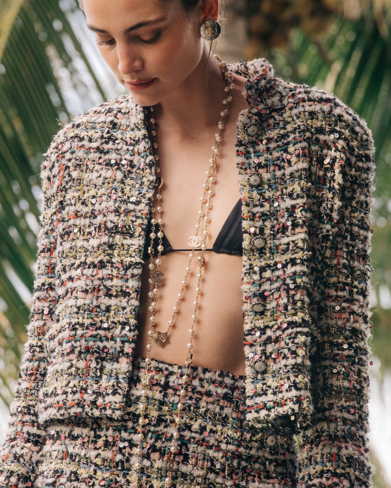 Model wearing Chanel tweed jacket with black bikini top and pearl necklace