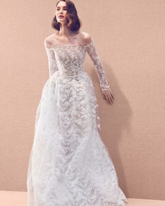 Long sleeve allover floral lace embroidered lace gown with tulle overskirt and featuring organza appliqués attached on to a base of ari embroidery threadwork for a 3-D effect, totaling 80 hours of work to complete.