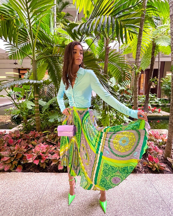 Versace blouse, Barocco mosaic-print pleated skirt, Purple Medusa bag, Palazzo dia crystal ring and pendant necklace and green heels from the SS21 collection.