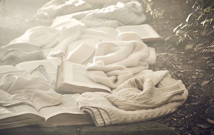 Brunello Cucinelli campaign image for Never Ending Stories with books and sweaters lining the ground of a forest.