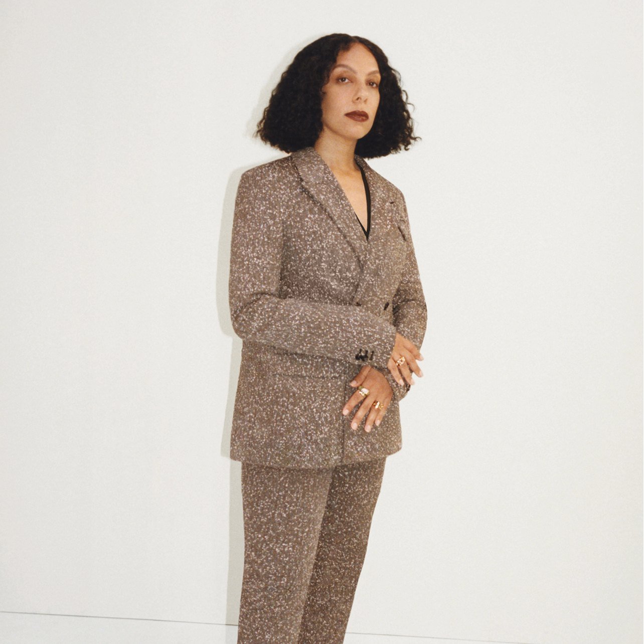 Woman poses wearing a brown pant suit with white speckled detailing