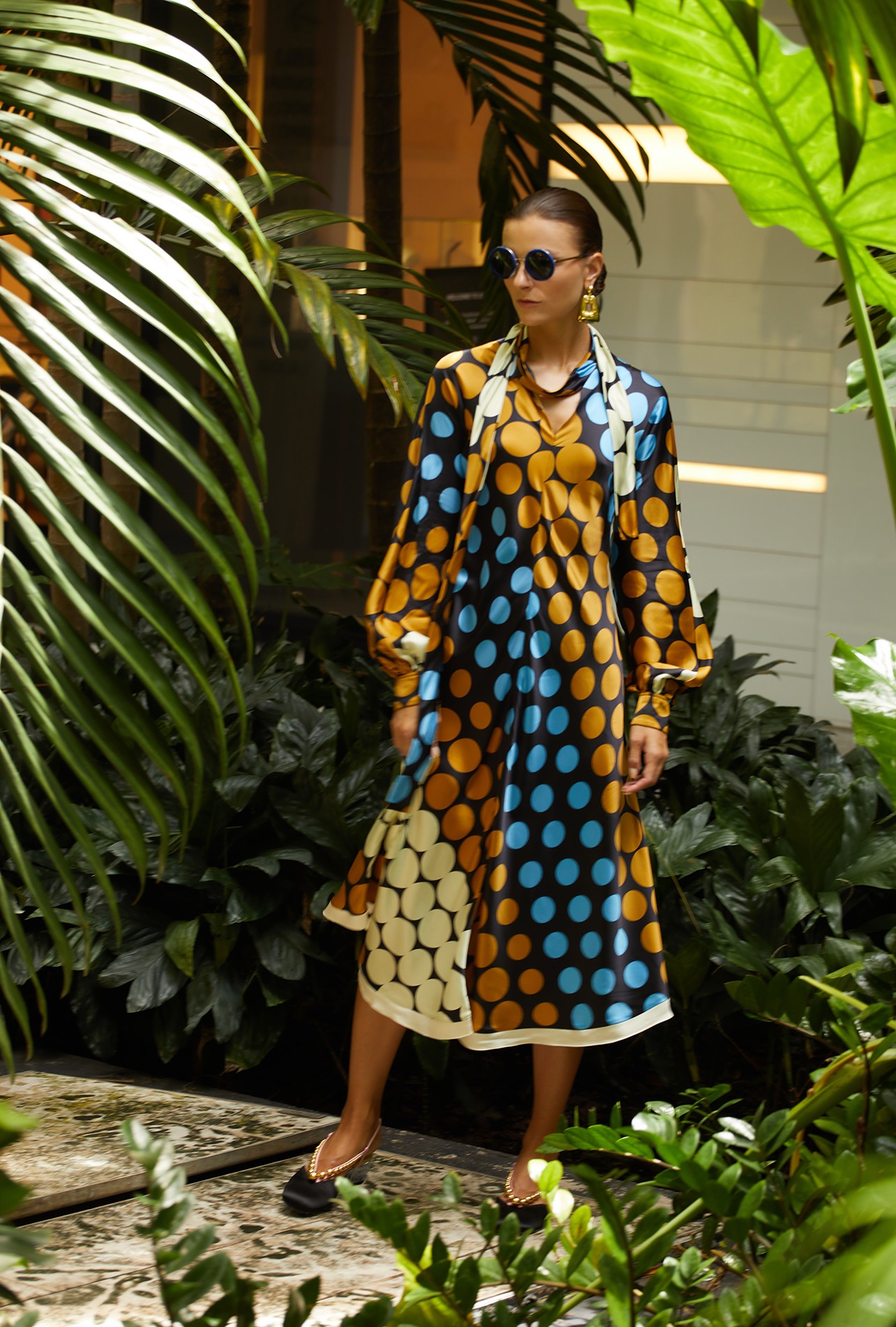 Blue, gold and ivory satin print dress with lavallière collar, black satin pump with low plexiglass heel and blue circle-framed sunglasses