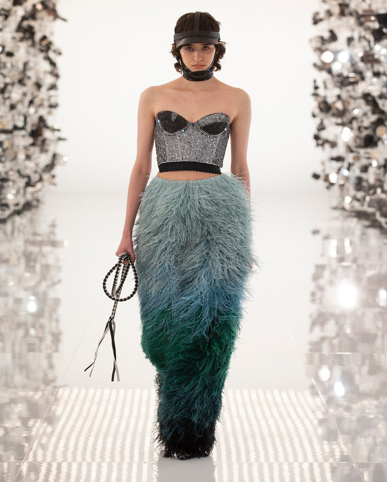 Woman walking on a runway in an embellished bustier crop top and a blue feathered skirt