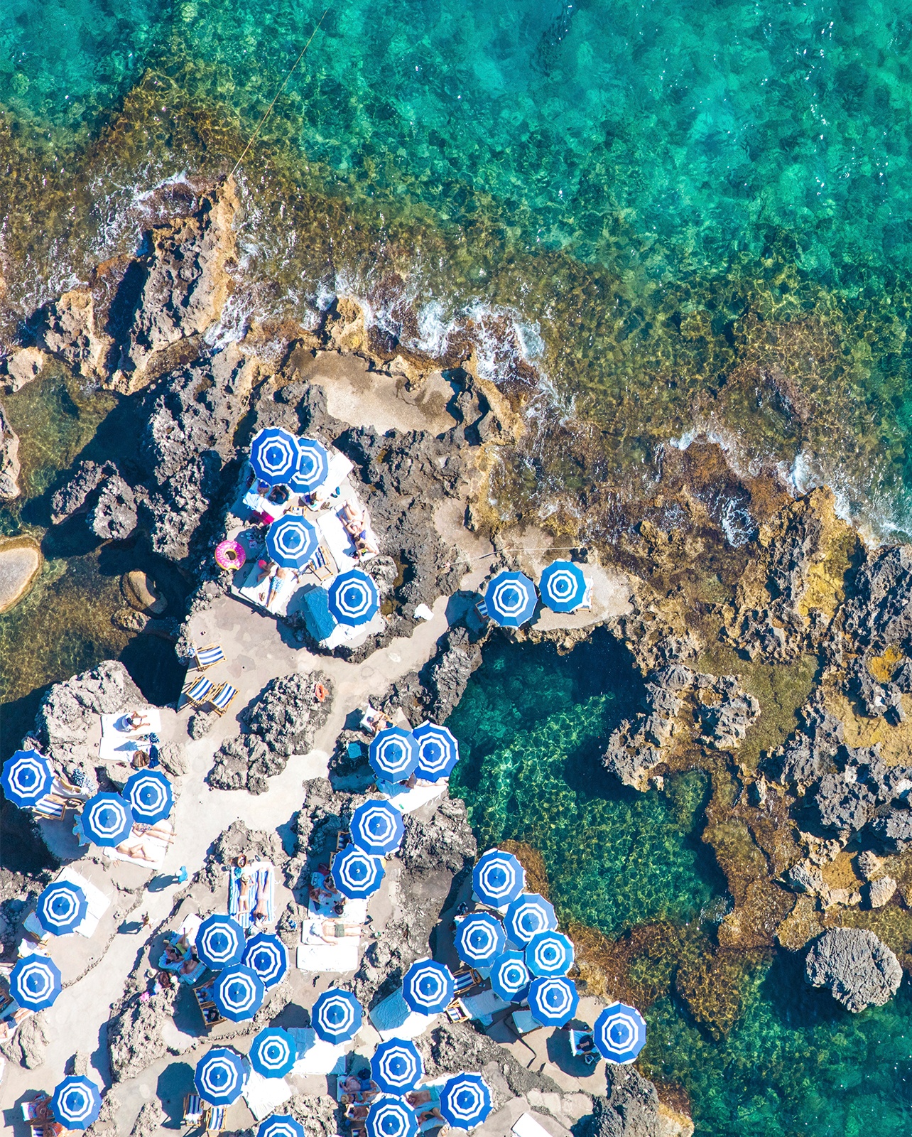 Arial photo of the Mediterranean coast with scattered blue umbrellas