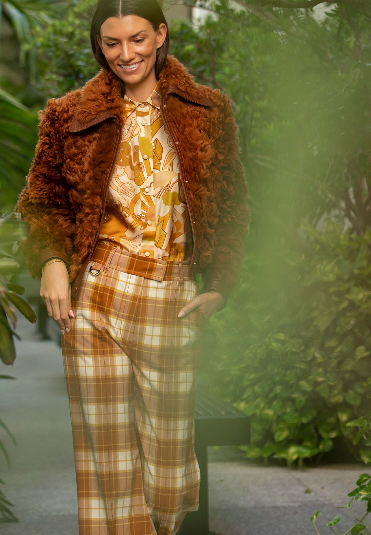 Woman is walking with a smile wearing a retro-style blouse, plaid trousers and a shearling jacket from Zimmermann