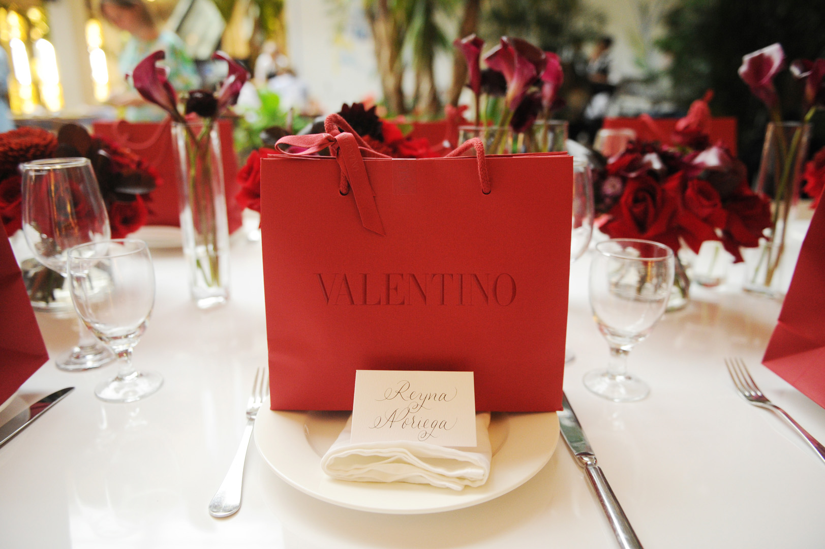 A dining placement with a handwritten name card and a red Valentino shopping bag