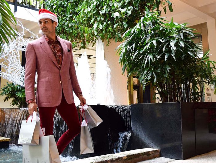 Male model in burgundy suit walking through Bal Harbour Shops with Neiman Marcus shopping bags.