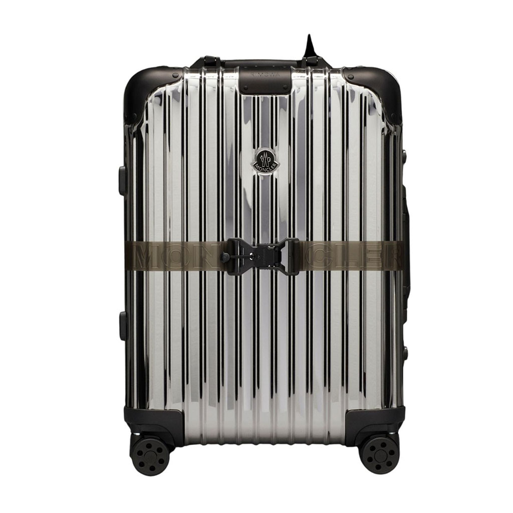 Silver hard shell cabin size suit case with exterior Moncler strap.