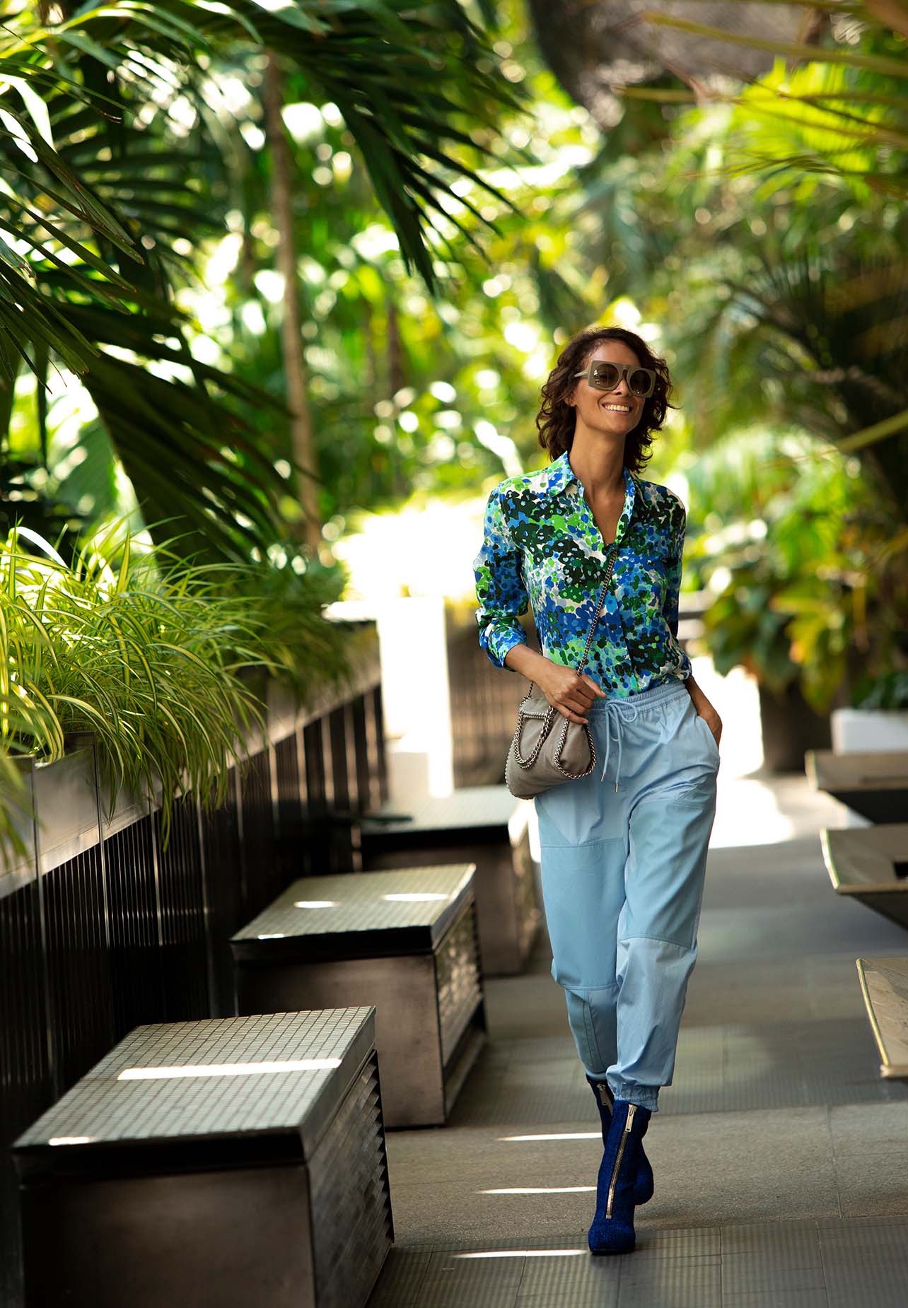 Woman smiles in a floral blouse and blue Stella McCartney trousers