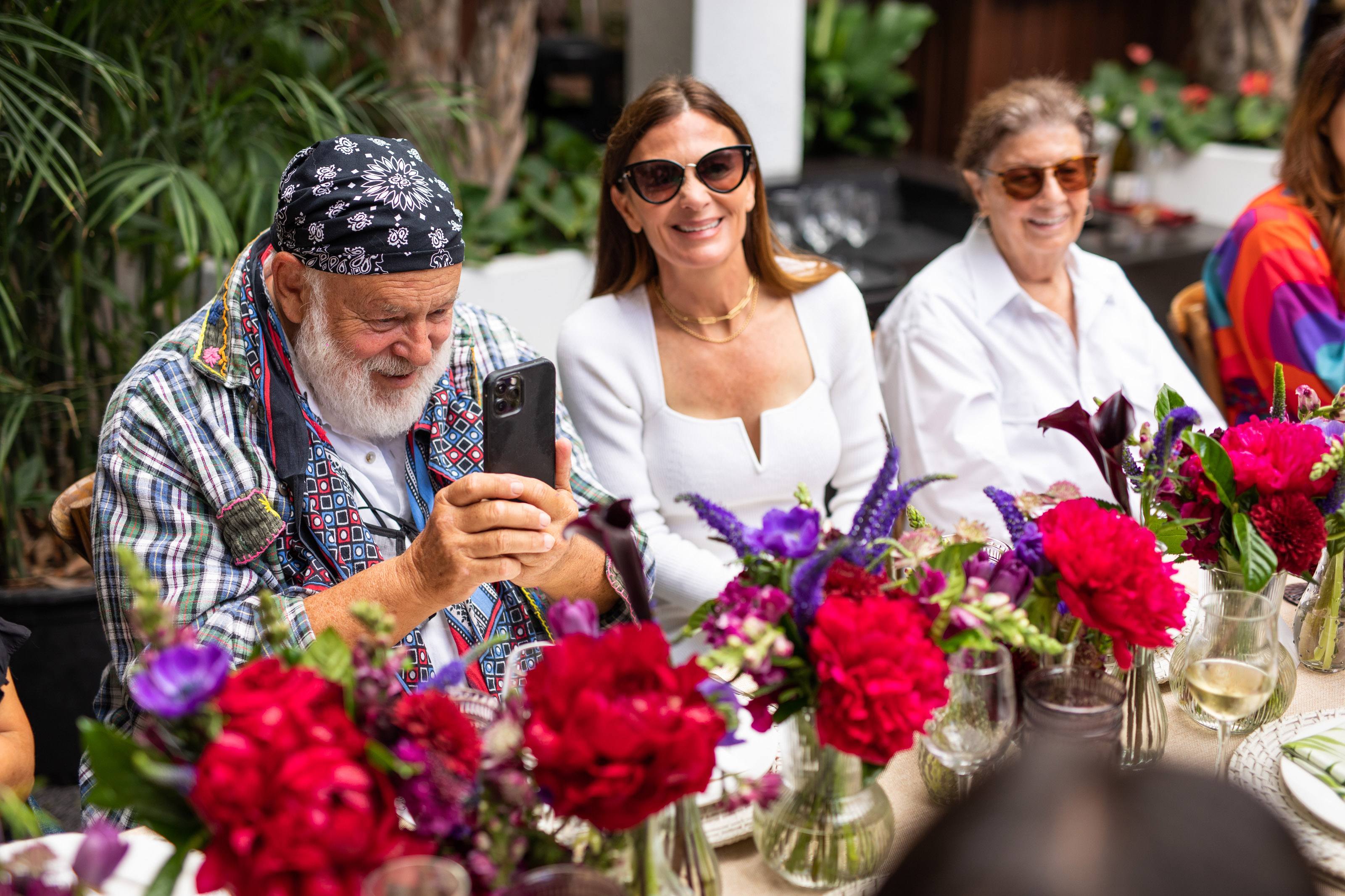 Bruce weber snaps a photo on his phone and Sarah harrelson smiles next to him