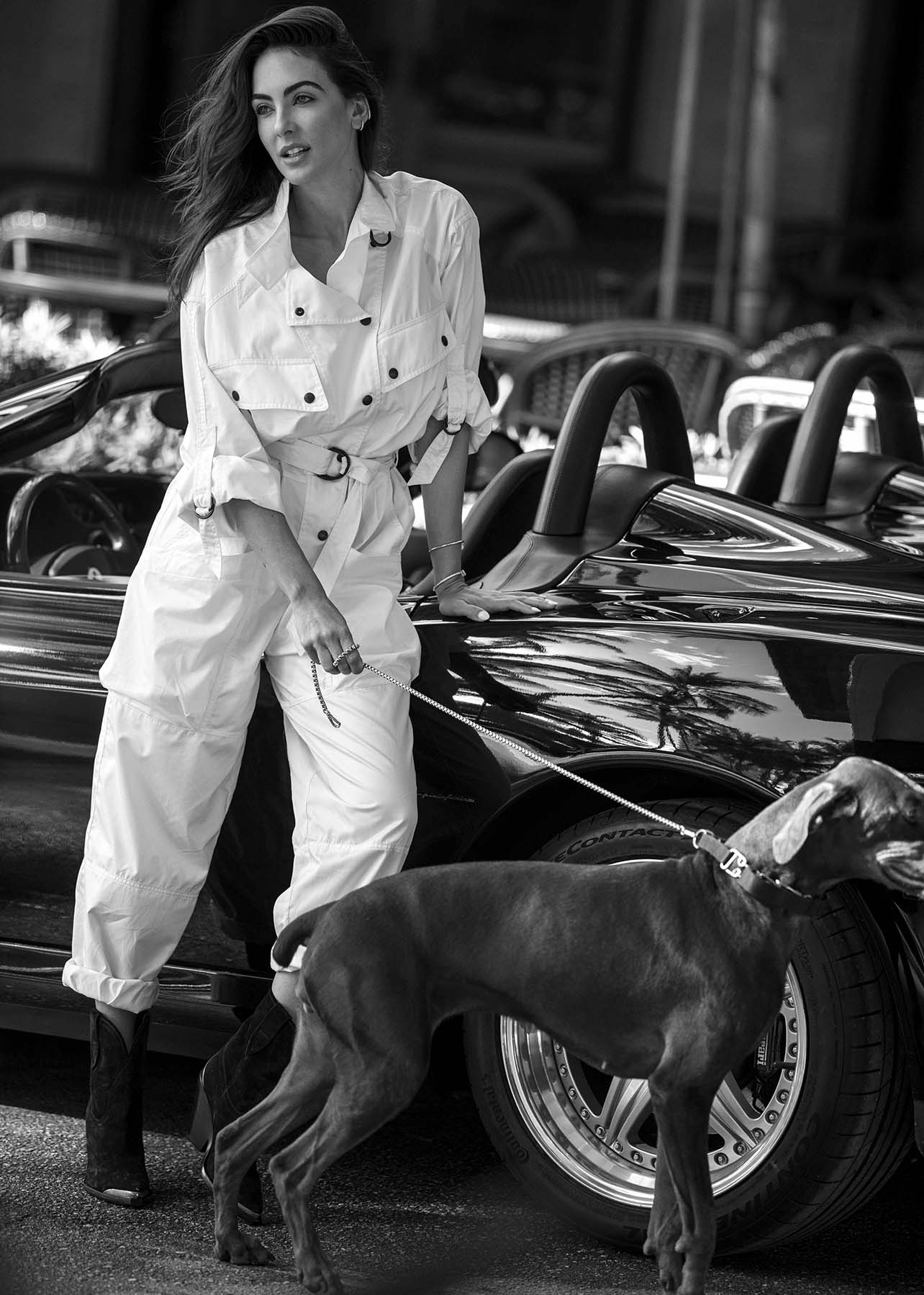 Model poses in front of a sports car pulling a dog on a leash