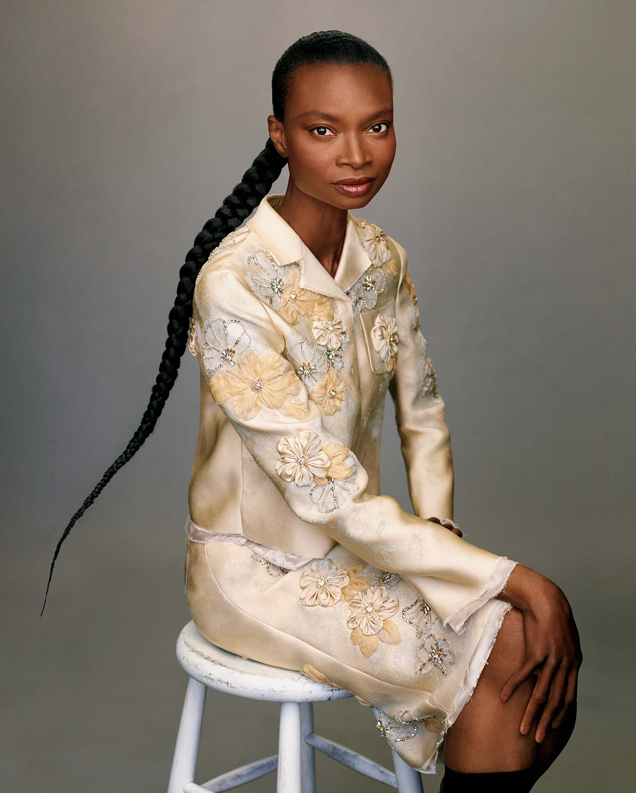 Model sits on a stool in a cream jacket and skirt
