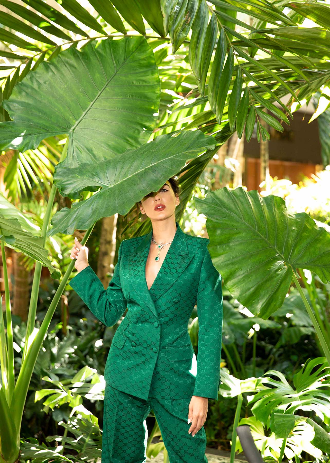 Model stands behind a palm tree in a full Gucci emerald suit