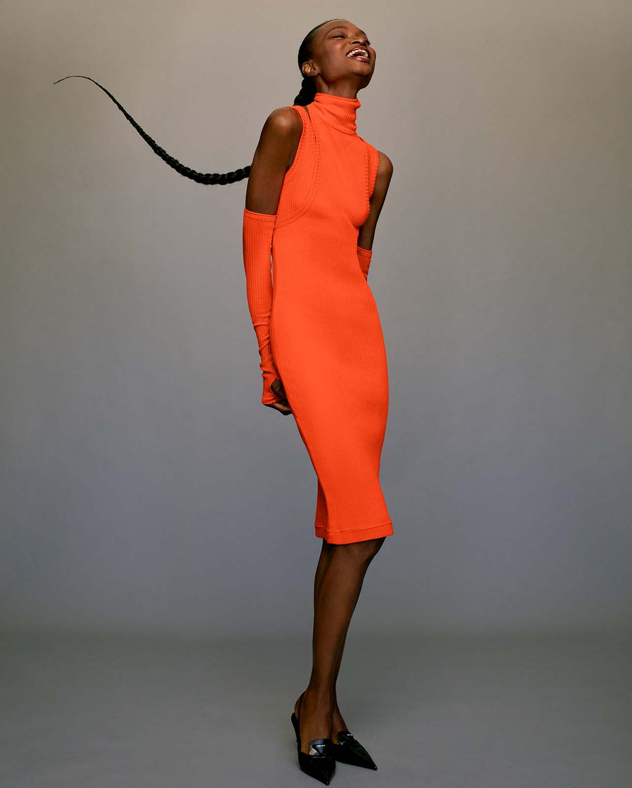 Model smiles in a high neck orange midi dress and black flats