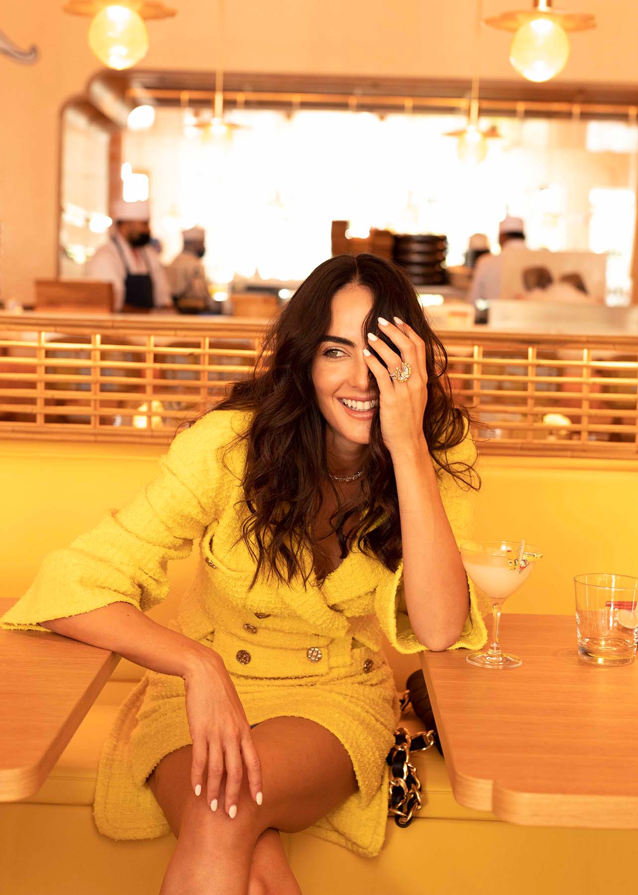 Model smiles while sitting in Makoto in a yellow tweed Chanel set