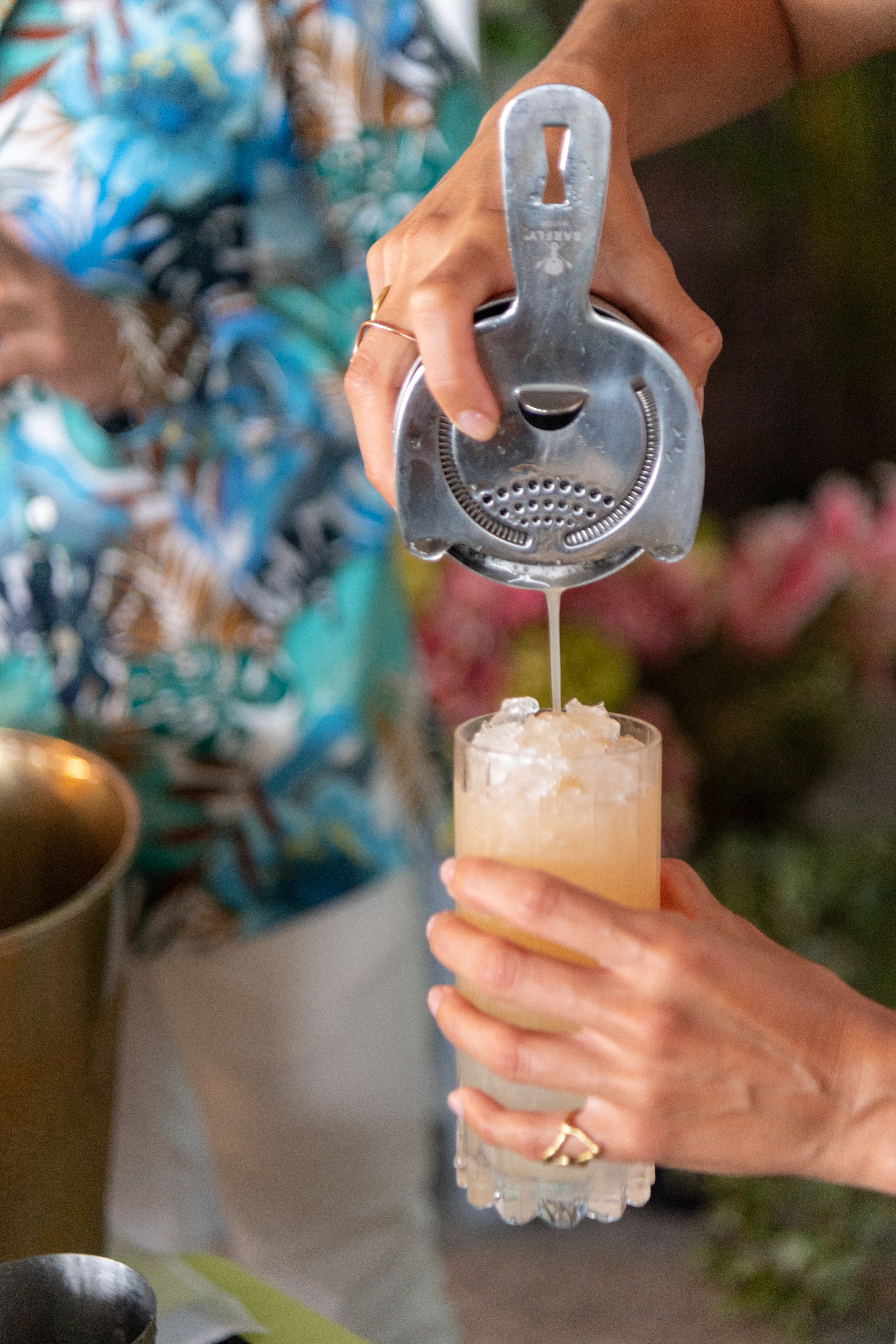 Woman pouring a cocktail into a glass from a metal cocktail shaker