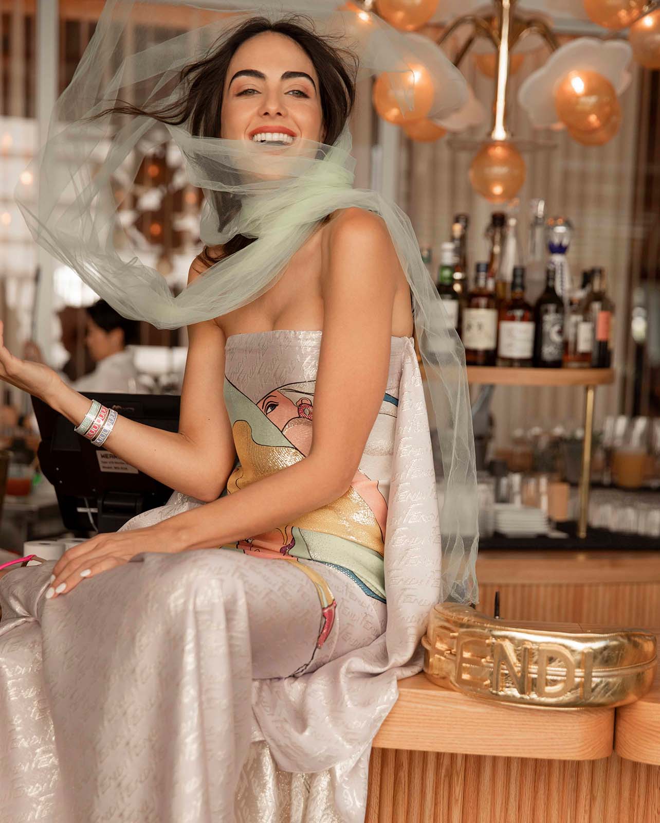 model smiles in a multicolored fendi dress, sitting on top of a bar
