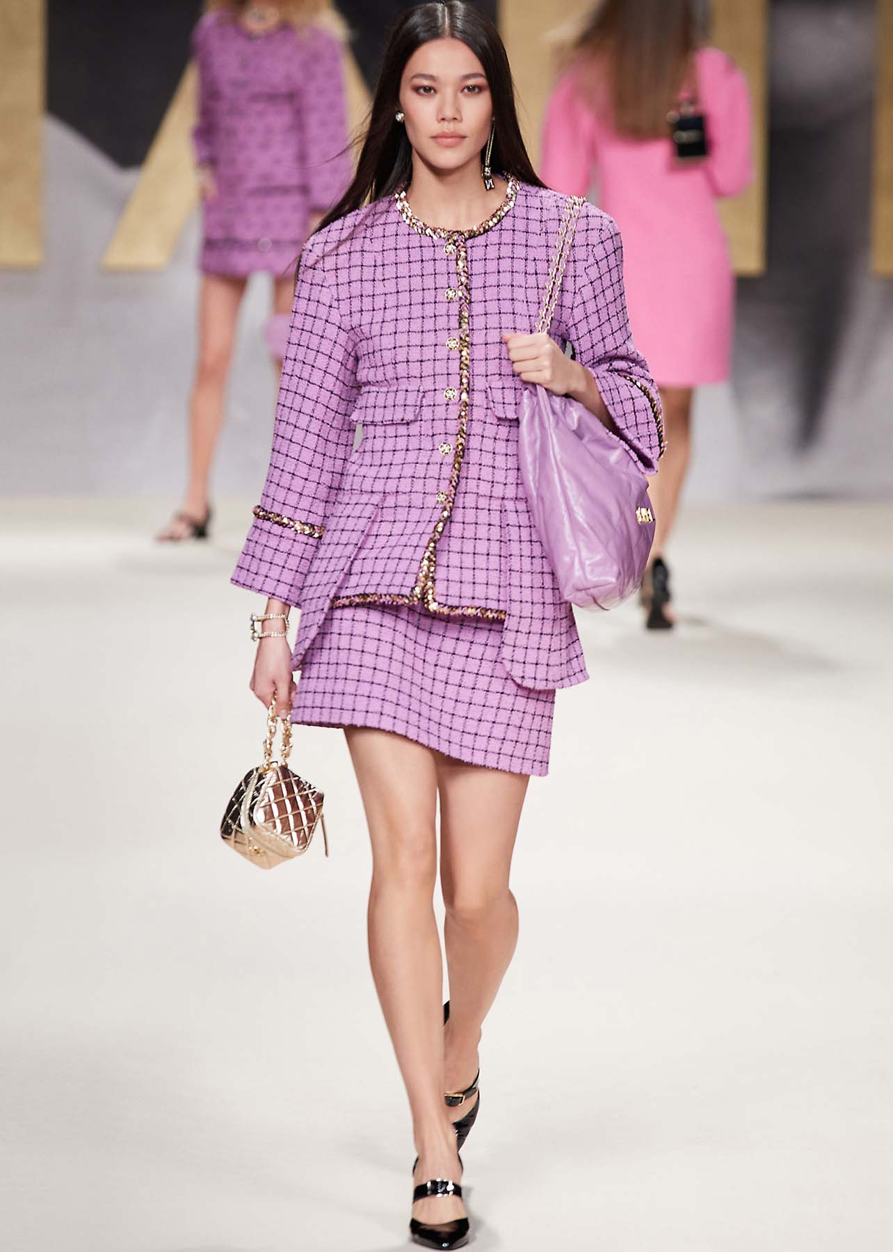 Model walking a runway in a purple tweed jacket and skirt