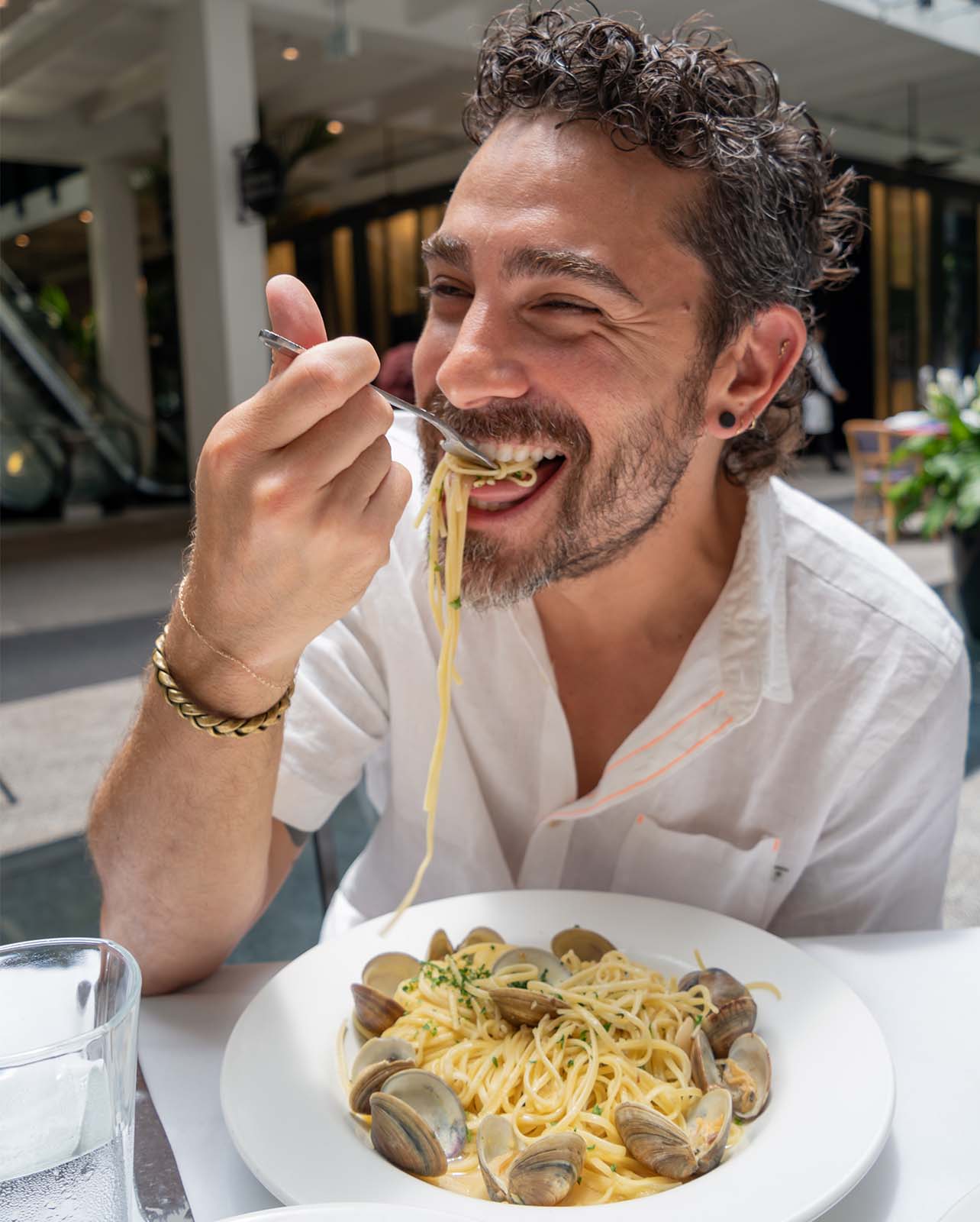 Man smiles while eating a bite of pasta