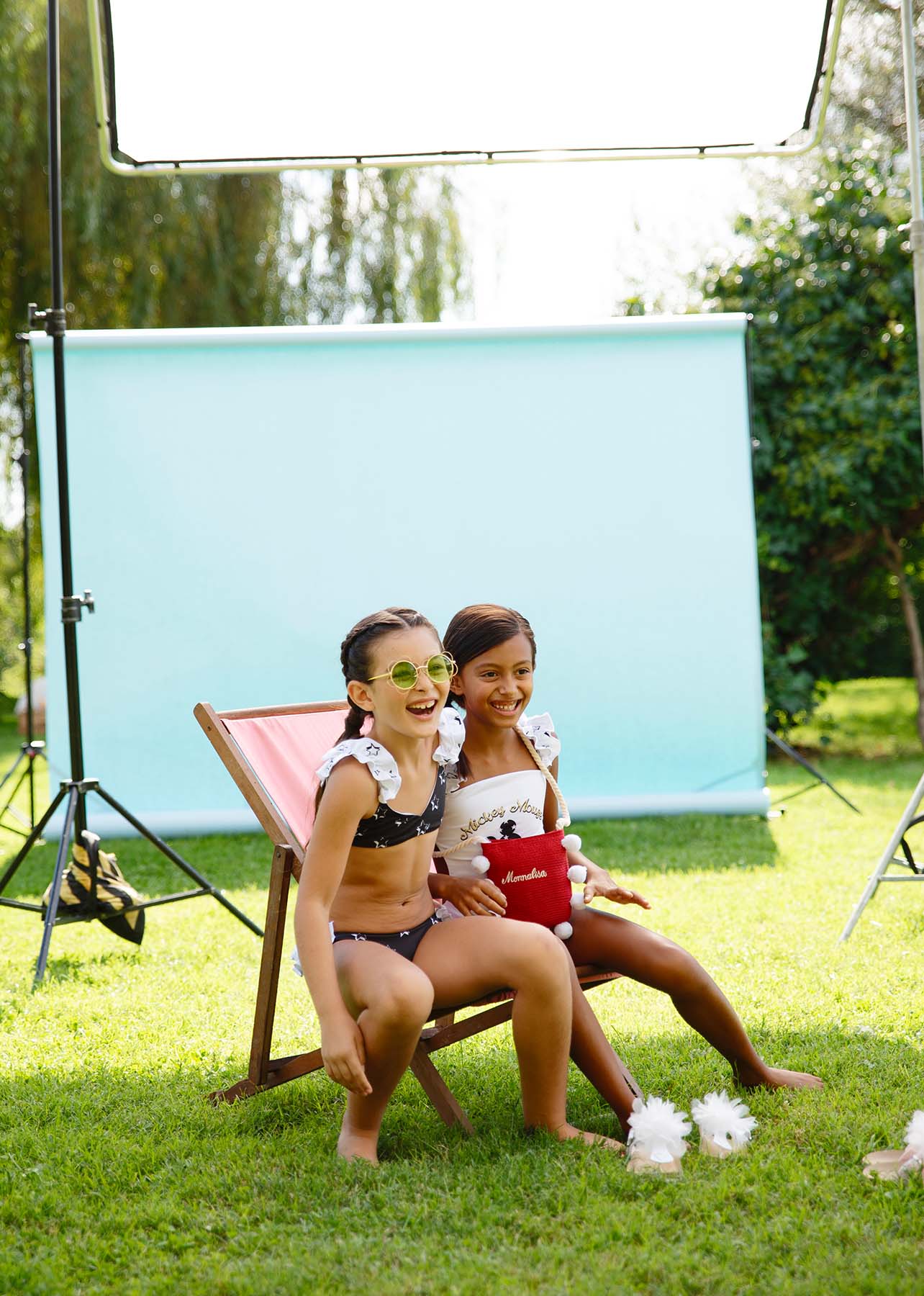 two children smile wearing bikinis sitting outside