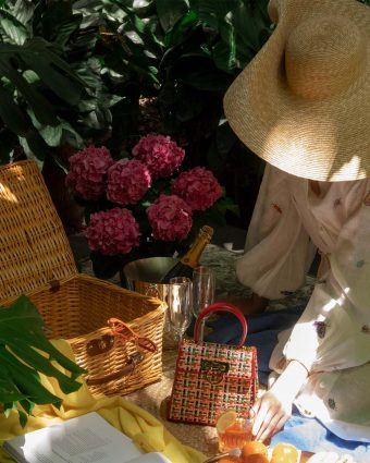 model wears a white sundress and sun hat surrounded by picnic accessories