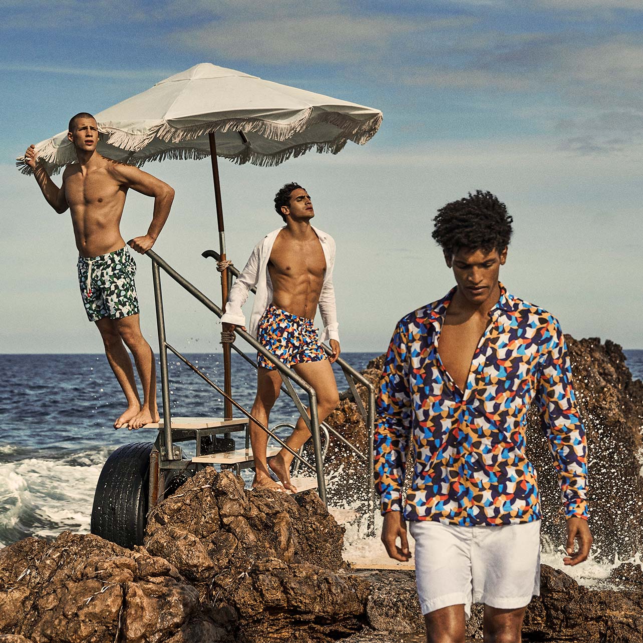 Three male models pose in swim trunks and button down shirts