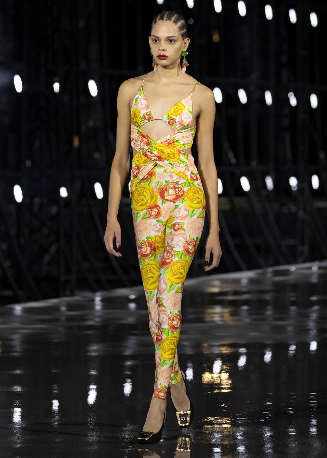 Model walks a runway in a yellow floral print jumpsuit