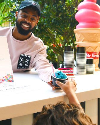 Man working at an ice cream vendor booth hands a child a cup of ice cream