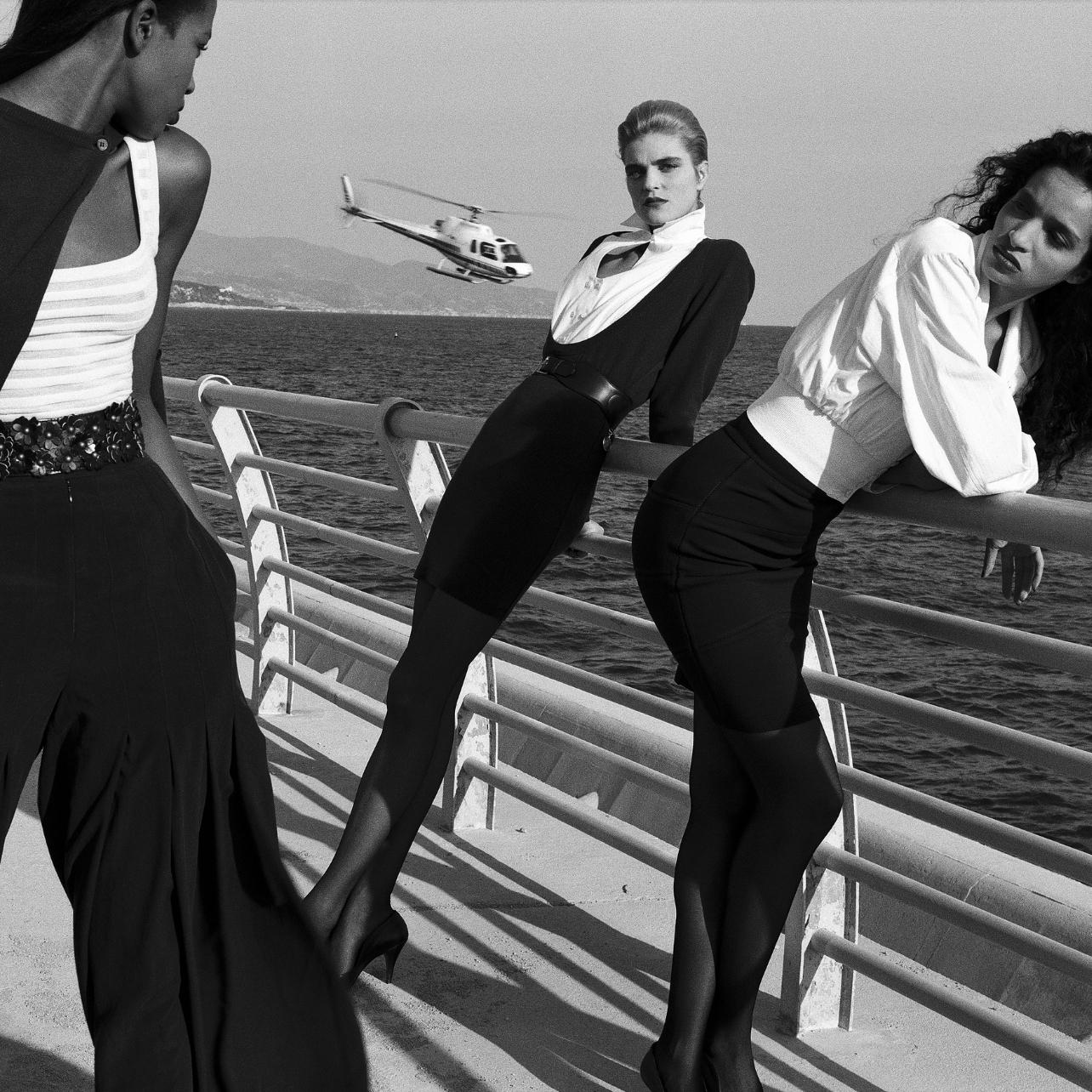 Black and white image of three models on a barge overlooking the water dressed in black and white looks designed by Alaïa.