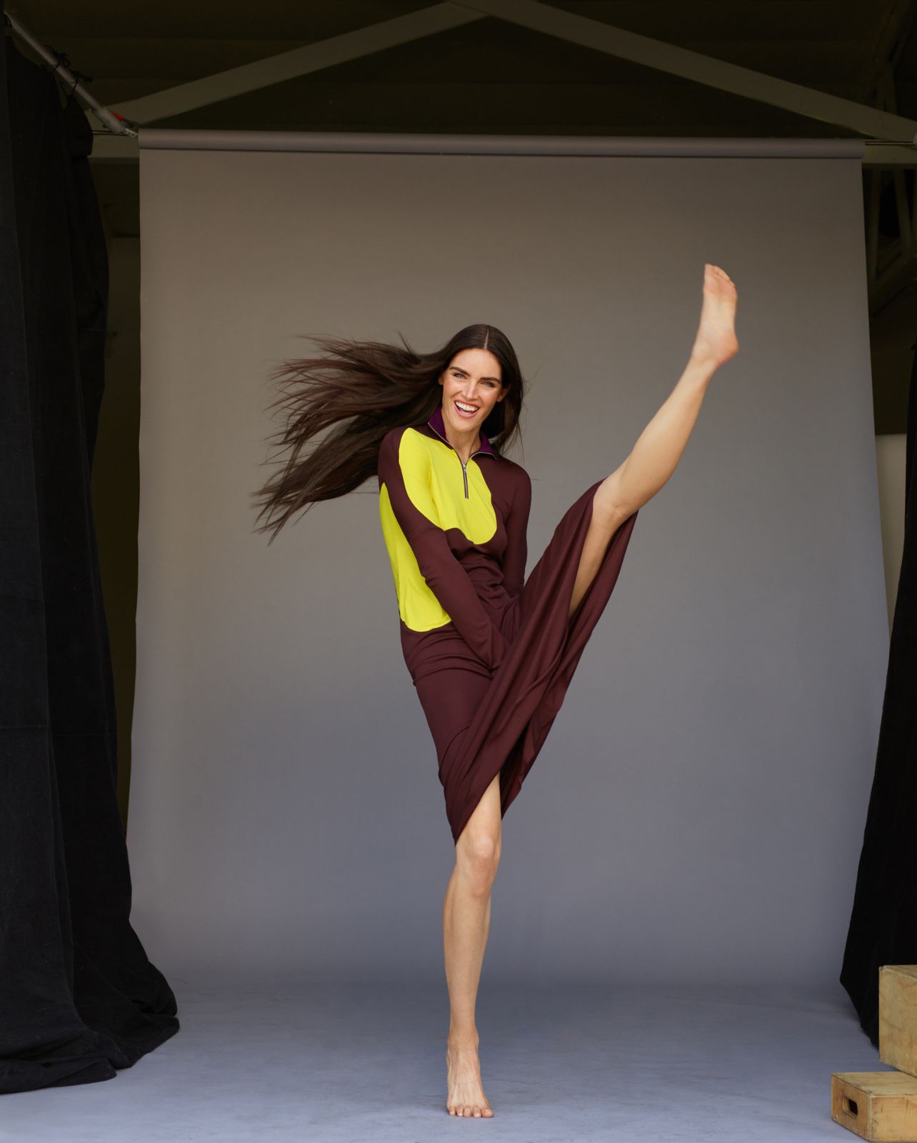 Model pictured kicking her leg up in the air wearing a long sleeve sweater dress