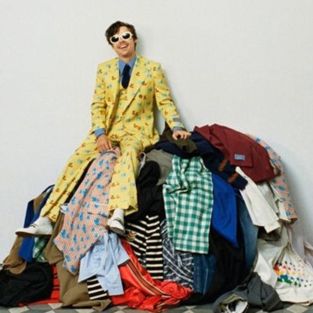 Harry Styles in a yellow suit sitting on top of a pile of clothes from the Gucci HA HA HA collection