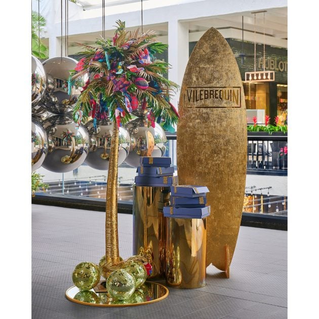 Gold surf-inspired holiday installation featuring a surfboard, palm tree with holiday décor