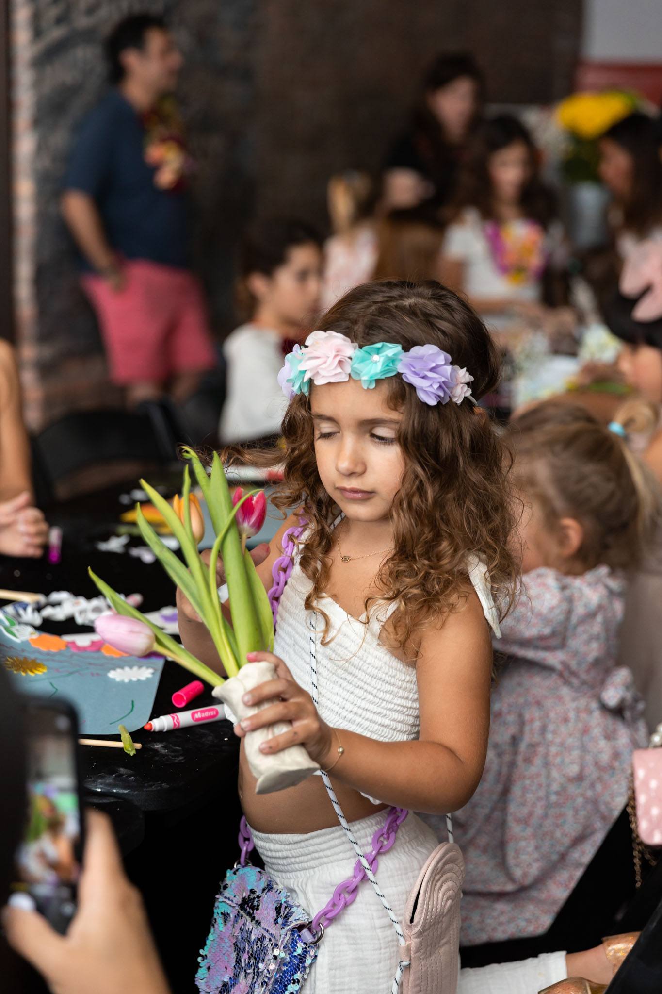 Child wearing a floral crown and admiring her clay floral vase