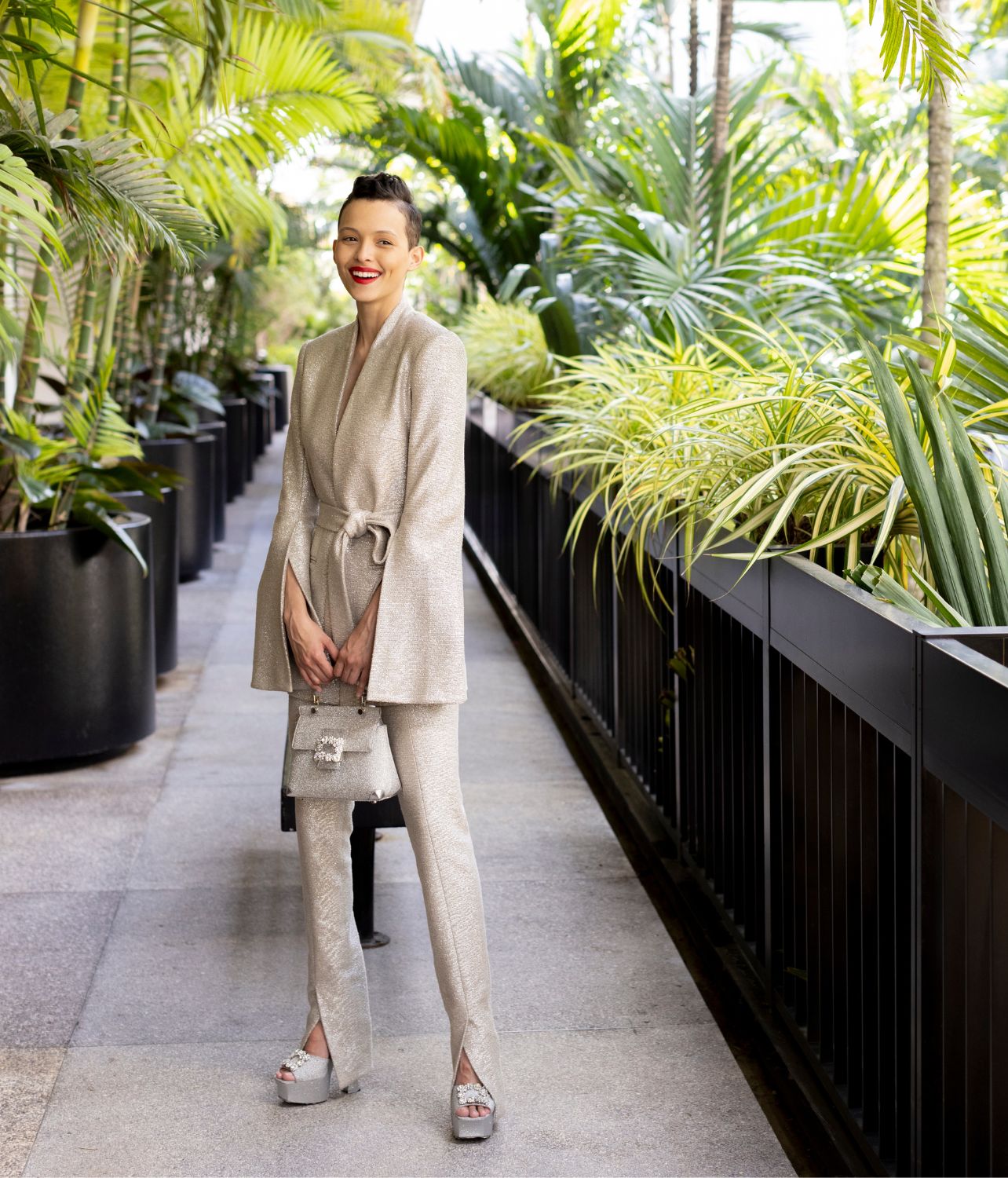 Model Camila Bueno waves at the camera wearing a silver Zimmermann blazer and pant set