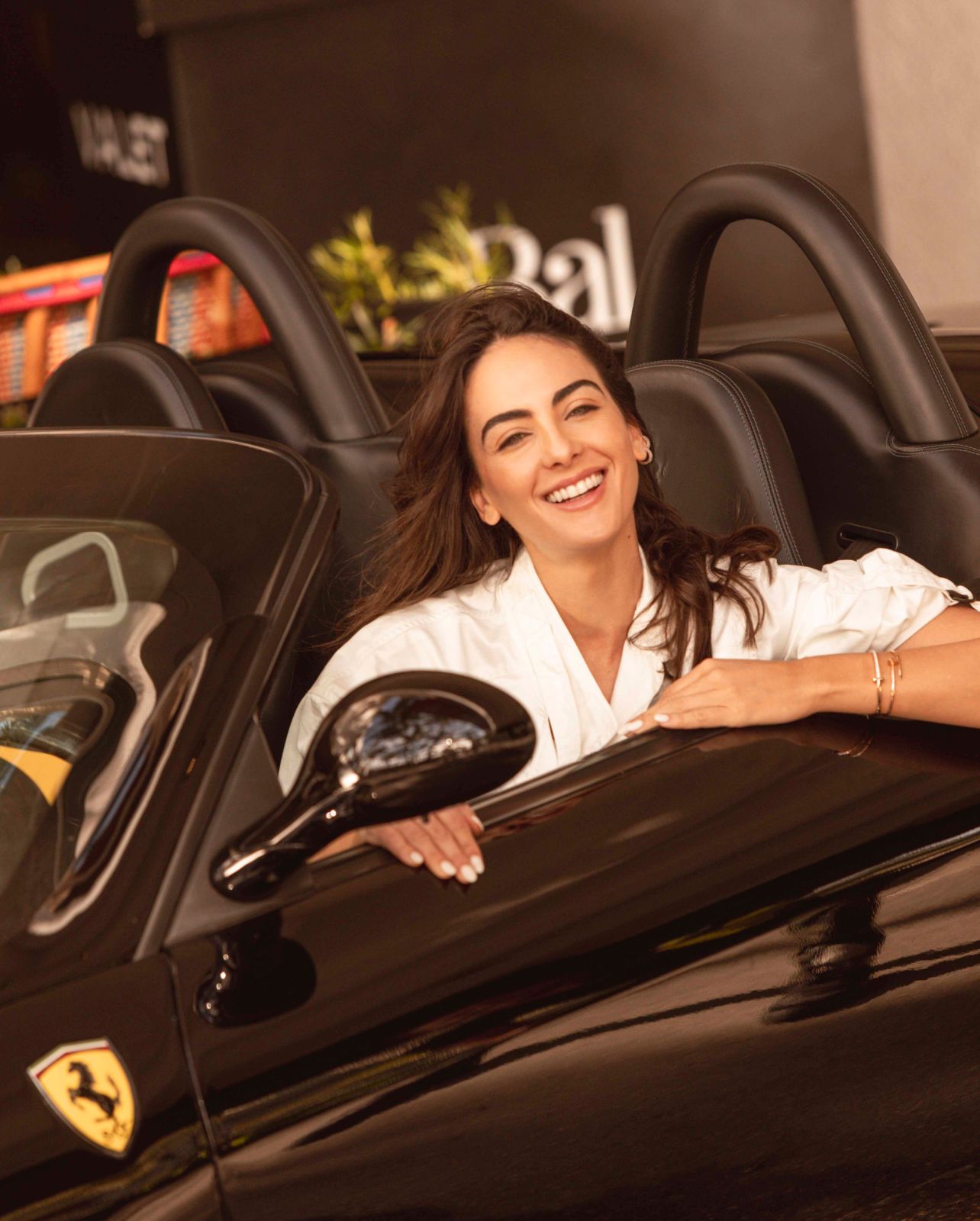 Model Daniela Botero sitting in black convertible Ferrari wearing a white Isabel Marant jumpsuit