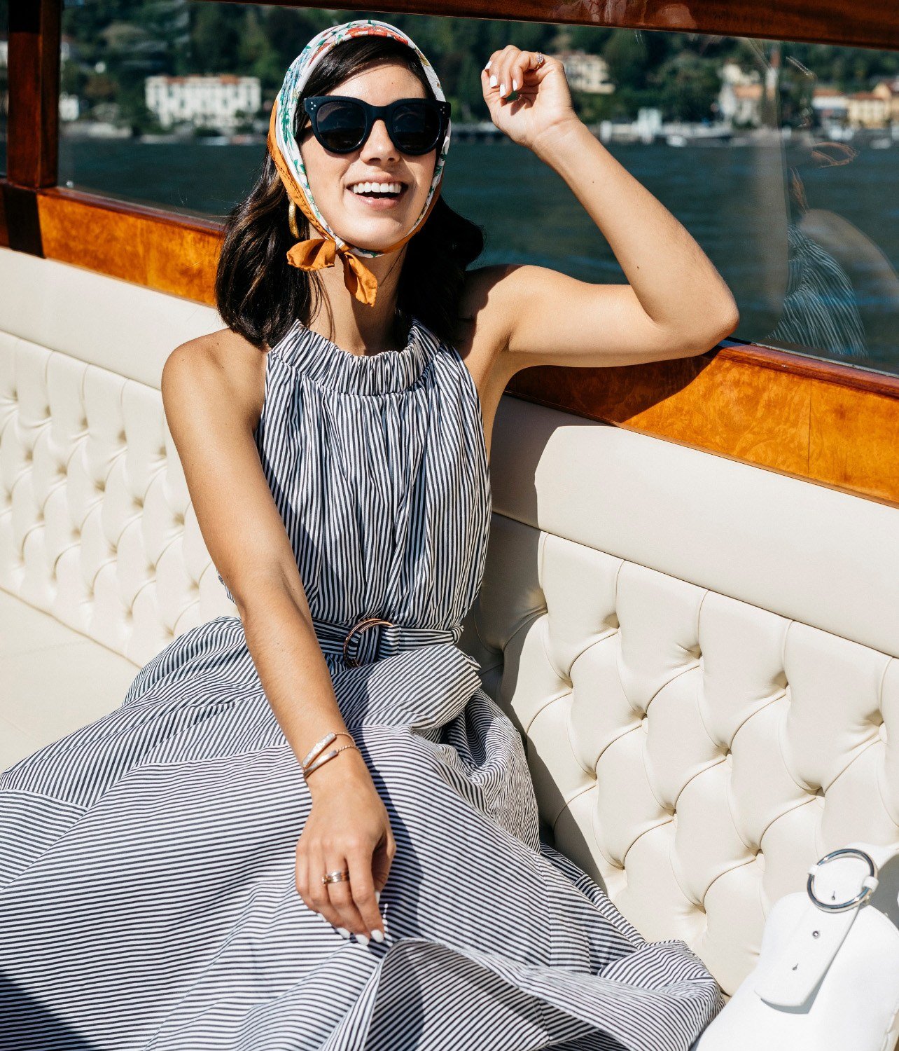 Model on a boat in Lake Como wearing a striped dress, headscarf, and sunglasses