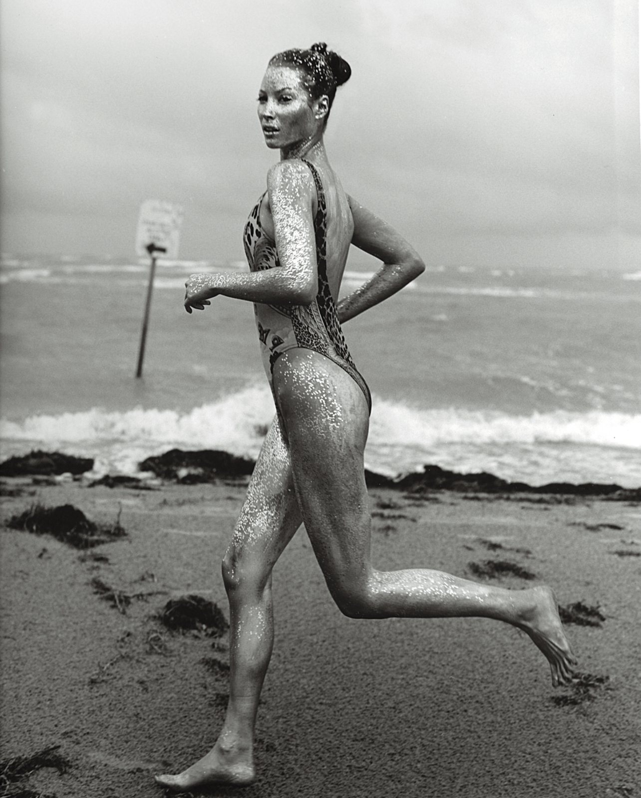 Model Christy Turlington wearing one piece bathing suit running along the beach