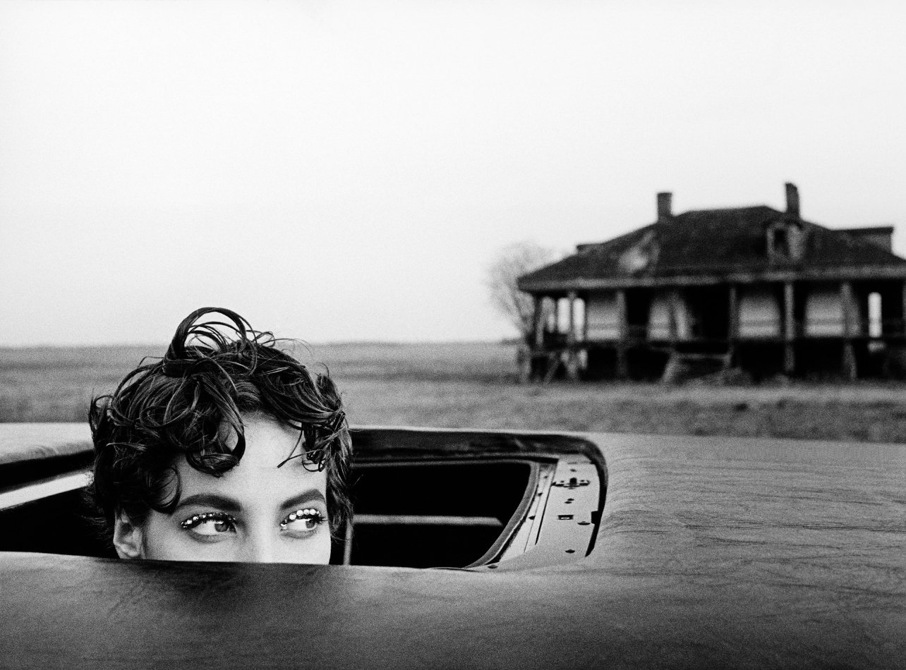 Black and white portrait of Christy Turlington posed in the sunroof with gem eyeliner