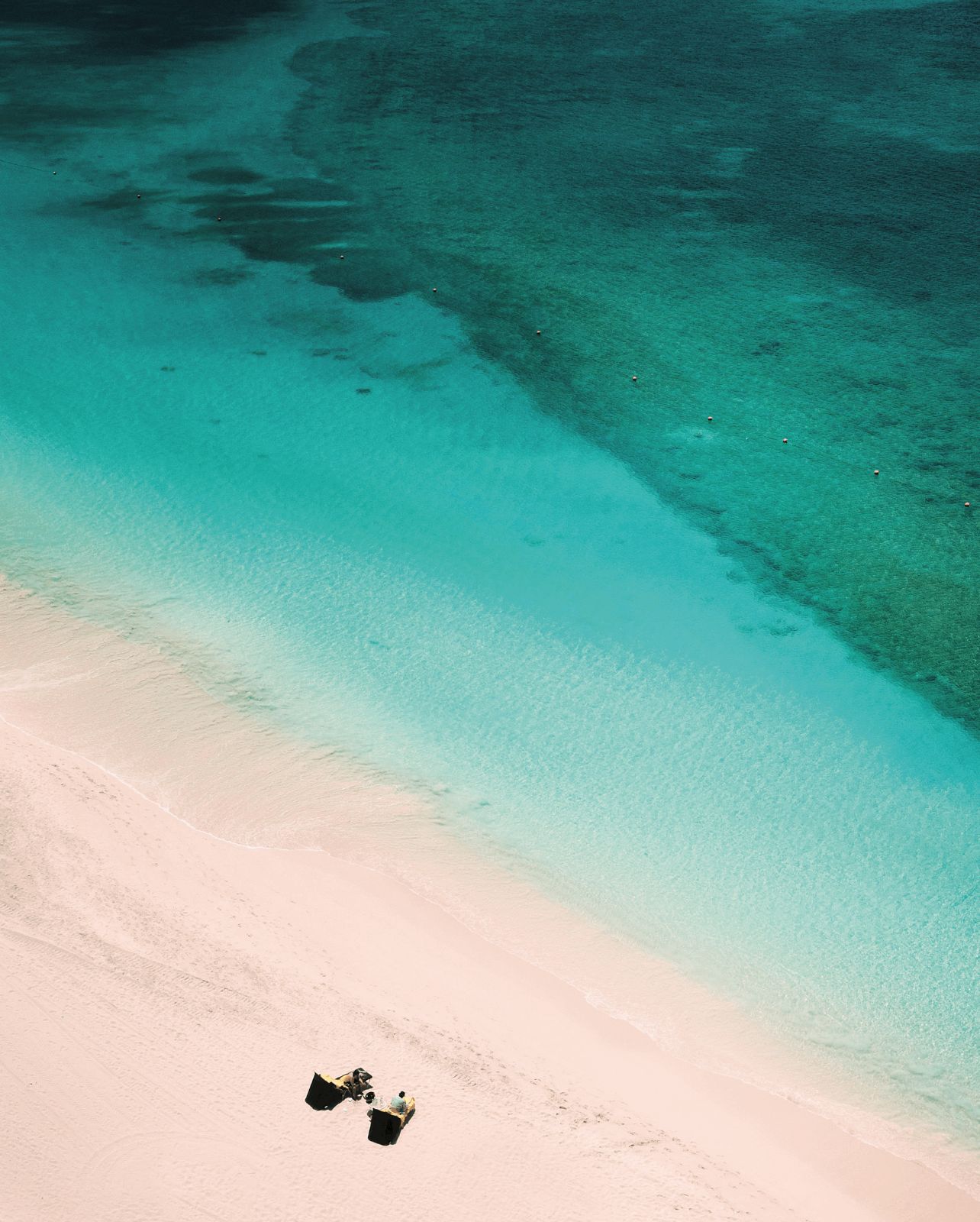 Bird’s-eye-view of the beach and ocean with two people in lounge chairs