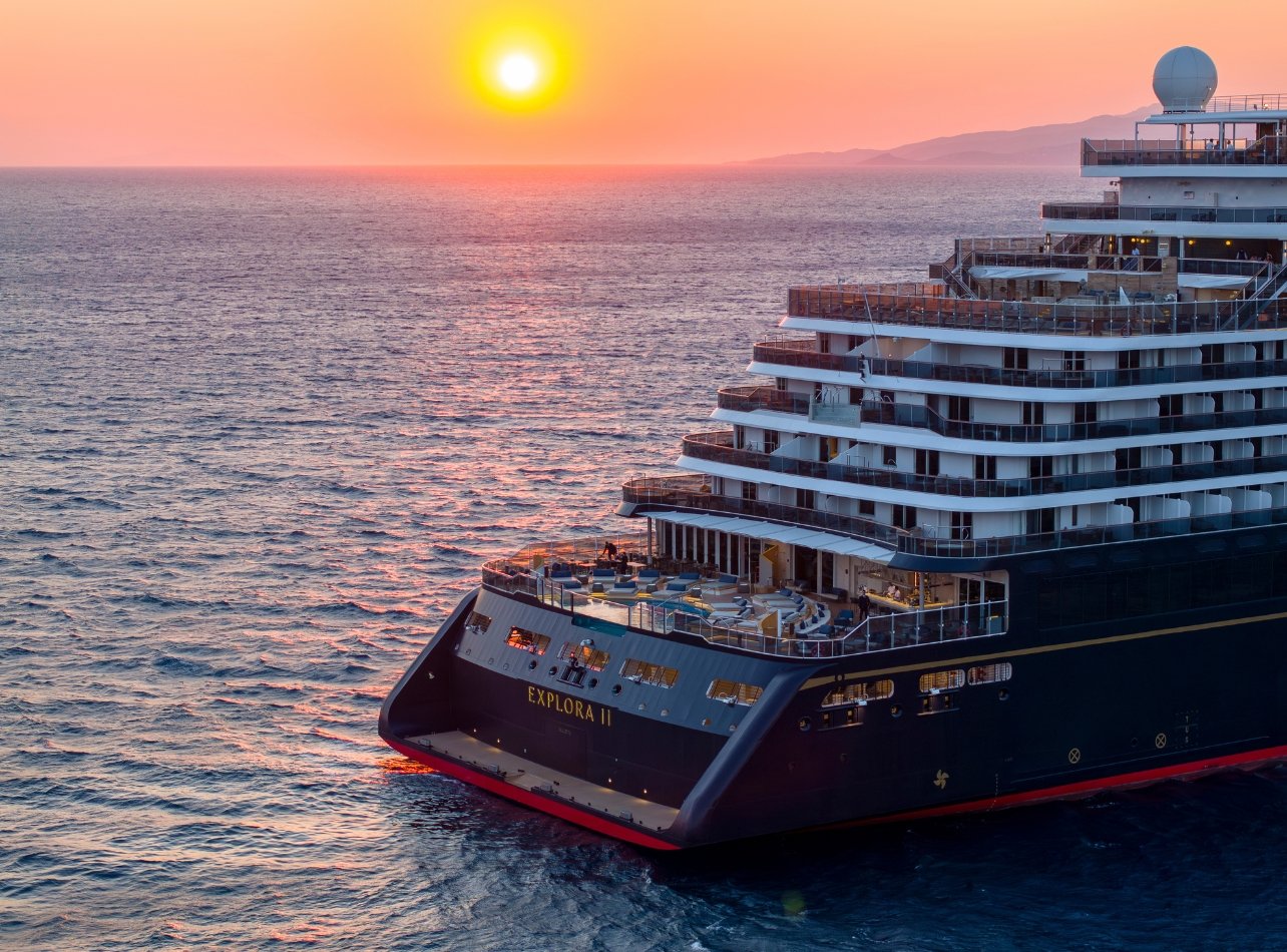 Back of the Explora Journeys II ship in the middle of the ocean with sunset in the background