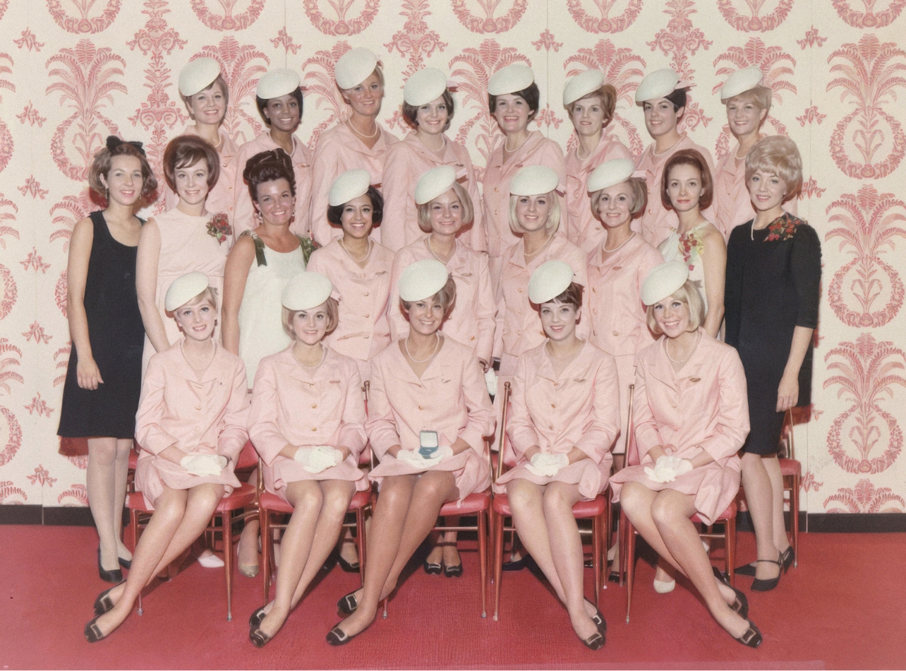 A group of Women posed for a photo wearing pink suit uniforms, white hats, pearls, and matching black shoes