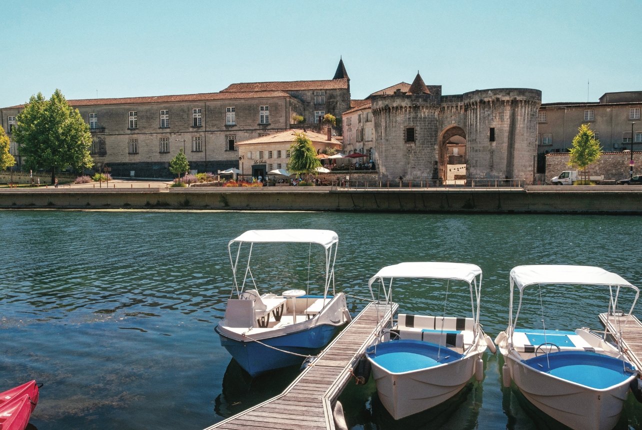 Scenic view of the Saint-Jacques Gate along the Charente River, with boats on the water and historic buildings nearby