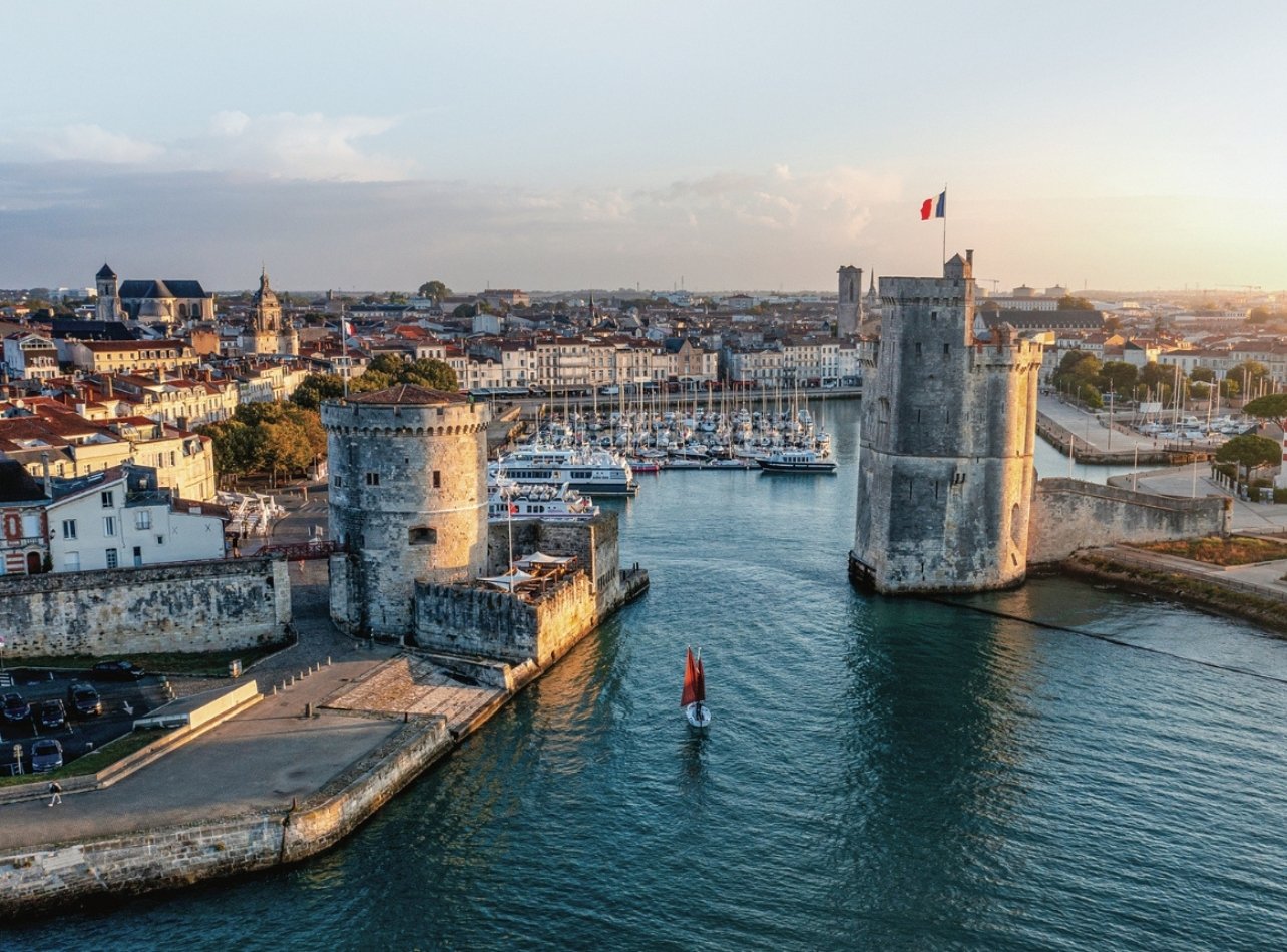 Sunset view of La Rochelle’s historic seaport, featuring boats in the harbor and old town buildings in the background
