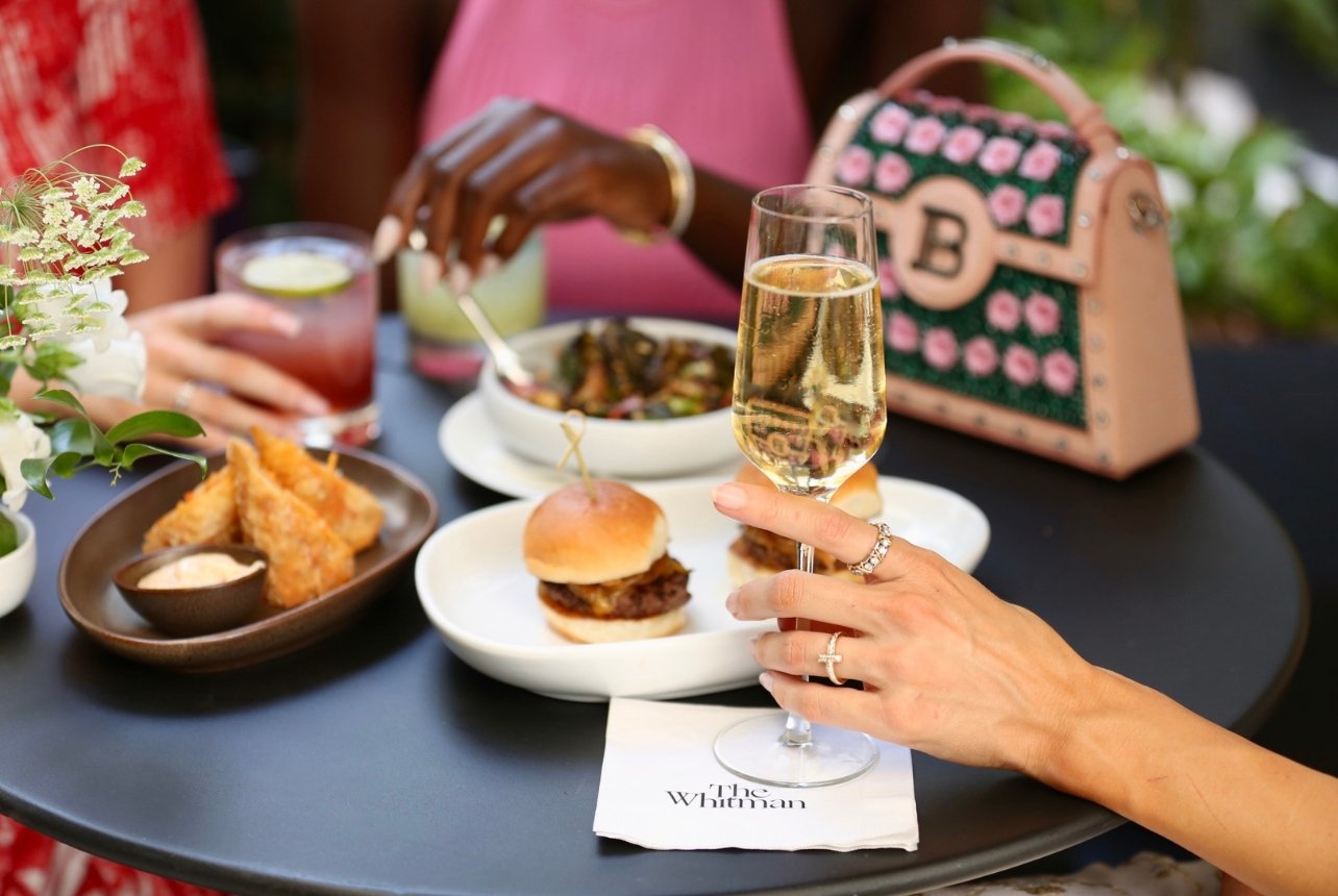 An outdoor dining table at The Whitman restaurant set with a vibrant spread of food and drinks