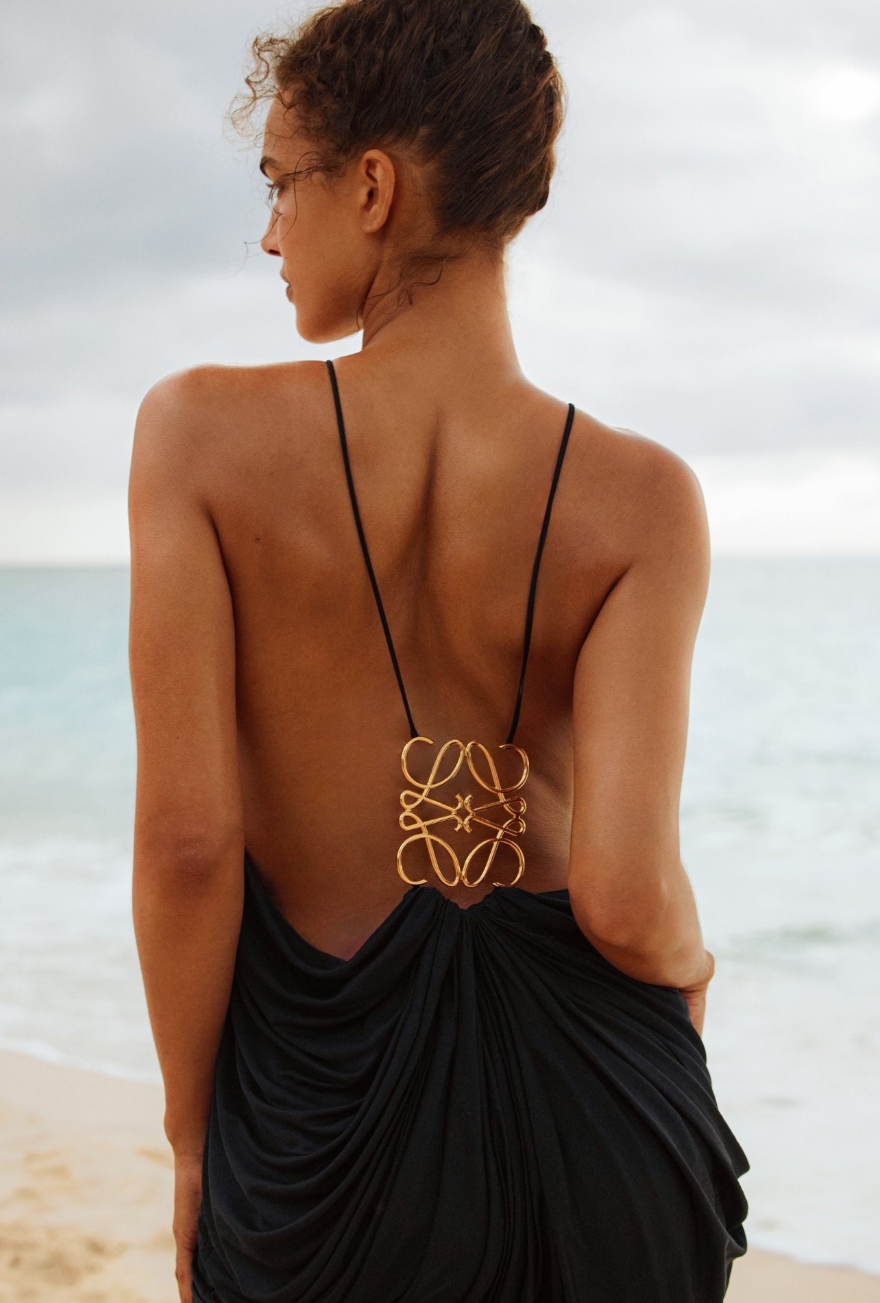 Fashion model wearing a strappy Loewe dress with gold detailing on a beach