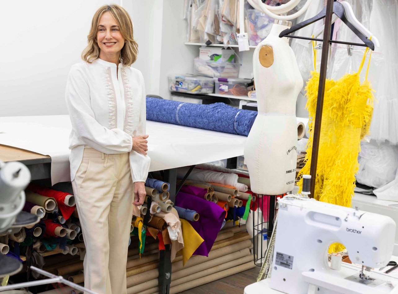 Silvia Tcherassi smiles for a portrait in her Coral Gables studio, surrounded by garment fabric, a sewing machine, and a mannequin