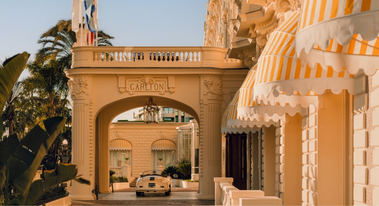 An exterior shot of the Carlton Cannes Hotel with a vintage car parked at the entrance
