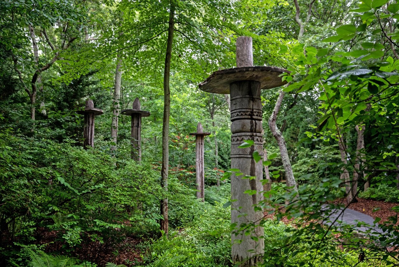 An installation of tall sculptures in the woods at the Indonesian house at the Watermill Center