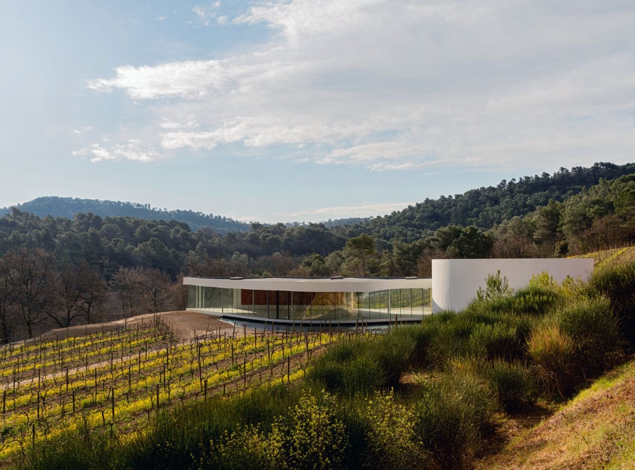Glass house in the middle of vineyard and hills filled with greenery