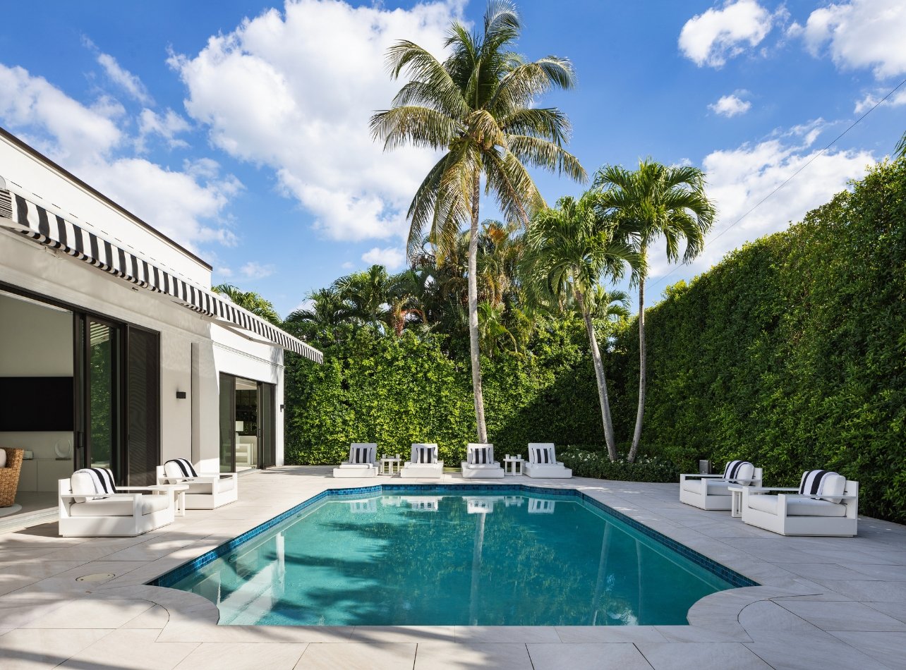 An inground pool in Palm Beach surrounded by lounge chairs, palm trees, and a large paved patio for entertaining